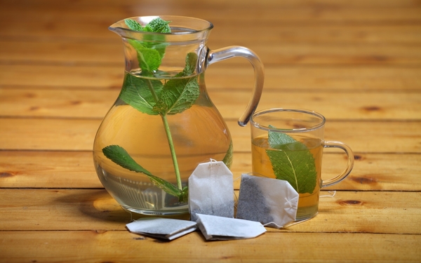 Jarra de vidrio con agua y hojas frescas sobre mesa clara
